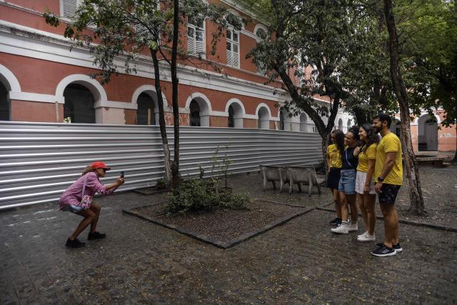 A group of tourists poses for a snapshot during a guided tour through the scenarios of the film "O Agente Secreto" (The Secret Agent) at the city center of Recife, Pernambuco state, Brazil, on February 13, 2026. The northeastern Brazilian city of Recife, where the Oscar-nominated movie "The Secret Agent" is set, is revelling in its moment in the limelight as tourists flock to film locations and a classic local shirt flies off the shelves. (Photo by BRENDA ALCANTARA / AFP)