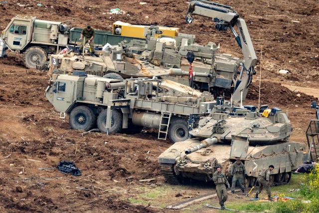Israeli soldiers work on the belts for their tanks at a staging area in the Upper Galilee in northern Israel near the border with Lebanon on March 13, 2026. Israel's defence minister on March 13, said Lebanon will suffer increasing damage to its infrastructure as Israel targets Hezbollah, after the military destroyed a bridge over the southern Litani river. (Photo by Odd ANDERSEN / AFP) / 