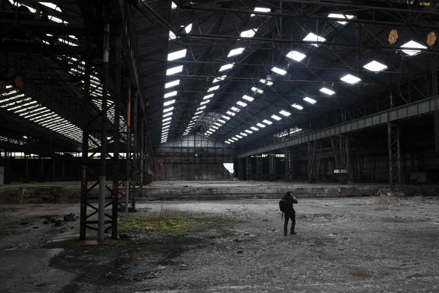 An urban explorer (urbex) walks as he takes photographs in the warehouse of an abandoned steel plant in Charleroi, southern Belgium, on February 9, 2026. Once a major industrial city of the coal industry, Charleroi still bears the marks of a working-class past now lying fallow. As they venture through its abandoned factories, urban explorers (urbex) end up telling the story of a system as much as of a pastime: that of a capitalism which pours investment into a place, exploits it, then withdraws, leaving behind nothing but ruins to explore. (Photo by Nicolas TUCAT / AFP)