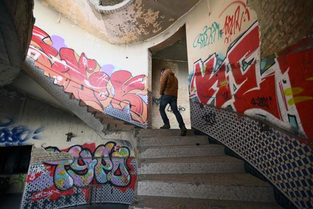 An urban explorer (urbex) climbs the stairs of an abandoned public swimming pool in Charleroi, southern Belgium, on February 9, 2026. Once a major industrial city of the coal industry, Charleroi still bears the marks of a working-class past now lying fallow. As they venture through its abandoned factories, urban explorers (urbex) end up telling the story of a system as much as of a pastime: that of a capitalism which pours investment into a place, exploits it, then withdraws, leaving behind nothing but ruins to explore. (Photo by Nicolas TUCAT / AFP)