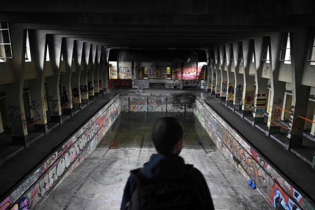 An urban explorer (urbex) scouts an abandoned public swimming pool in Charleroi, southern Belgium, on March 11, 2026. Once a major industrial city of the coal industry, Charleroi still bears the marks of a working-class past now lying fallow. As they venture through its abandoned factories, urban explorers (urbex) end up telling the story of a system as much as of a pastime: that of a capitalism which pours investment into a place, exploits it, then withdraws, leaving behind nothing but ruins to explore. (Photo by Nicolas TUCAT / AFP)