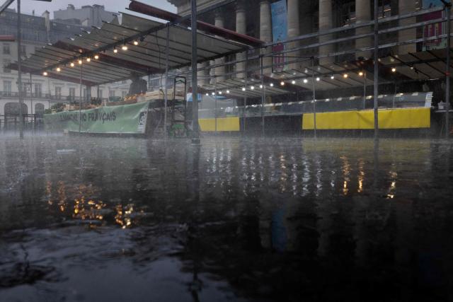 A vendor stands behind their fresh produce stall at a local market on a rainy day in Paris on March 13, 2026. (Photo by JOEL SAGET / AFP)