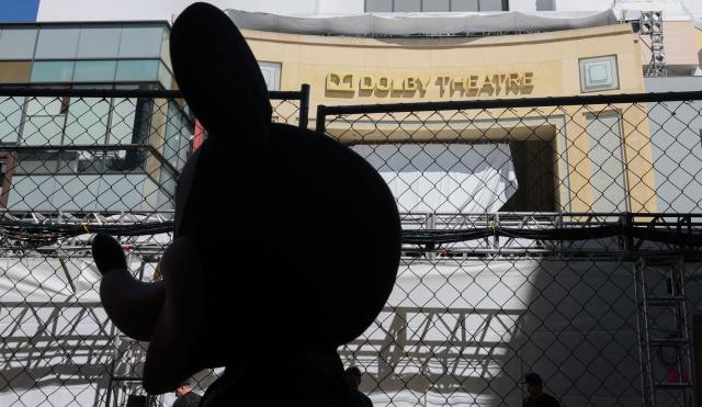 The silhouette of a street performer dressed as Mickey Mouse is seen in front of the Dolby Theatre as preparations are made ahead of the 98th Annual Academy Awards in Hollywood, California, on March 13, 2026. (Photo by ANGELA WEISS / AFP)