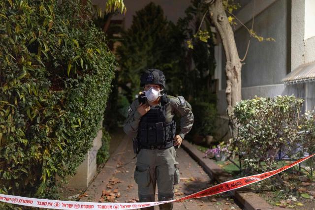 A member of Israel's security forces stands behind a police ribbon at a house that was reportedly hit by a projectile in Shoham  in central Israel, near Tel Aviv, on March 13, 2026. Smoke could be seen rising from two locations around Israel's commercial hub Tel Aviv on March 13, AFP journalists said, after blasts were heard following a warning that missiles were fired from Iran. (Photo by Ilia YEFIMOVICH / AFP) / 