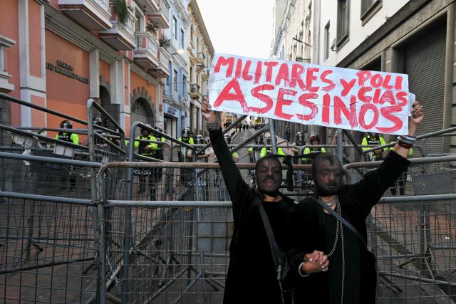 Demonstrators hold a sign that reads in Spanish "Military and Police, Murderers" as they perform in front of riot police officers during a march against the government called by unions in Quito on March 13, 2026. (Photo by Rodrigo BUENDIA / AFP)
