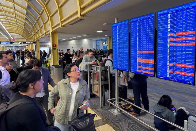 Travellers look at a departures screen inside a terminal during a ground stop at Ronald Reagan Washington National Airport in Arlington, Virginia, on March 13, 2026. Ground stops are in effect at three major DC-area airports due to a "strong odor coming from the Potomac TRACON" (Terminal Radar Approach Control) facility in Warranton, Virginia, according to a post on X by US Secretary of Transportation Sean Duffy. (Photo by Drew ANGERER / AFP)
