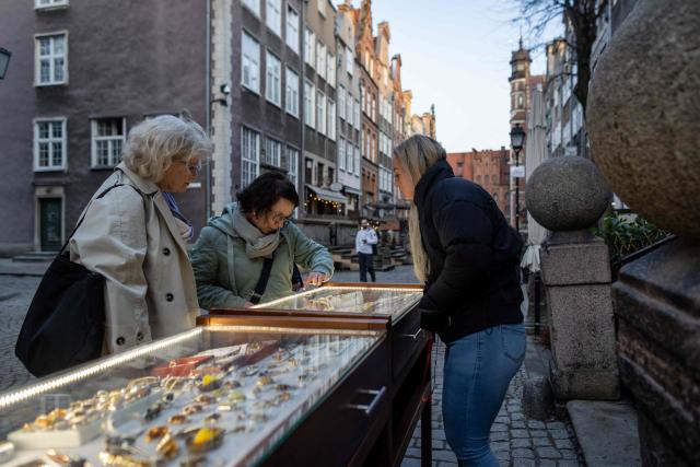 A vendor is offering necklaces and other jewellery made from natural Baltic amber at a stall outside the amber shop on Mariacka Street in Gda?sk, Poland on March 10, 2026. Long coveted for its golden color, scientific value and alleged healing properties, amber is now coming into the hand of young Polish jewelers, bringing the ancient resin into modern times. Together with drills, sanders, blasters, and power saws which look like they belong to a bygone era, virtual reality stations are used to combine earlier tools with state-of-the-art technology at the Academy of Fine Arts in Gdansk, a city on Poland's Baltic Coast known as amber's global capital. (Photo by Wojtek RADWANSKI / AFP)