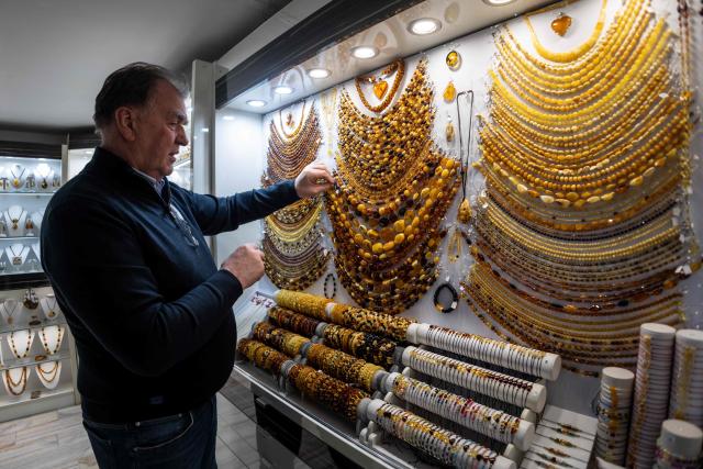 A vendor presents necklace made from natural Baltic amber at an amber shop on Mariacka Street in Gdansk, Poland on March 10, 2026. Long coveted for its golden color, scientific value and alleged healing properties, amber is now coming into the hand of young Polish jewelers, bringing the ancient resin into modern times. Together with drills, sanders, blasters, and power saws which look like they belong to a bygone era, virtual reality stations are used to combine earlier tools with state-of-the-art technology at the Academy of Fine Arts in Gdansk, a city on Poland's Baltic Coast known as amber's global capital. (Photo by Wojtek RADWANSKI / AFP)