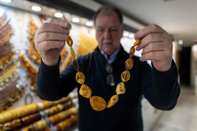 A vendor presents necklace made from natural Baltic amber at an amber shop on Mariacka Street in Gdansk, Poland on March 10, 2026. Long coveted for its golden color, scientific value and alleged healing properties, amber is now coming into the hand of young Polish jewelers, bringing the ancient resin into modern times. Together with drills, sanders, blasters, and power saws which look like they belong to a bygone era, virtual reality stations are used to combine earlier tools with state-of-the-art technology at the Academy of Fine Arts in Gdansk, a city on Poland's Baltic Coast known as amber's global capital. (Photo by Wojtek RADWANSKI / AFP)