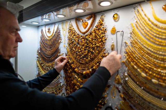 A vendor presents necklace made from natural Baltic amber at an amber shop on Mariacka Street in Gdansk, Poland on March 10, 2026. Long coveted for its golden color, scientific value and alleged healing properties, amber is now coming into the hand of young Polish jewelers, bringing the ancient resin into modern times. Together with drills, sanders, blasters, and power saws which look like they belong to a bygone era, virtual reality stations are used to combine earlier tools with state-of-the-art technology at the Academy of Fine Arts in Gdansk, a city on Poland's Baltic Coast known as amber's global capital. (Photo by Wojtek RADWANSKI / AFP)