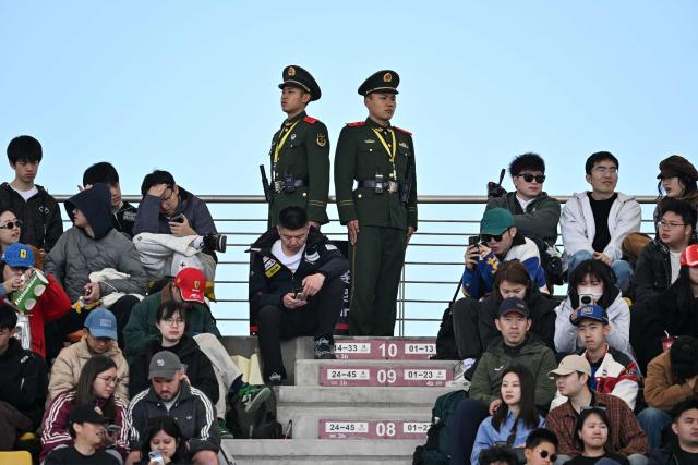 Spectators use their phones as they wait before the start of the qualifying session ahead of the Formula One Chinese Grand Prix at the Shanghai International Circuit in Shanghai on March 14, 2026. (Photo by HECTOR RETAMAL / AFP)