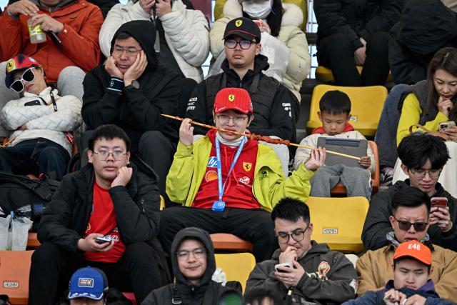 A fan (C) of team Ferrari enjoys a kebab skewer before the start of the qualifying session ahead of the Formula One Chinese Grand Prix at the Shanghai International Circuit in Shanghai on March 14, 2026. (Photo by HECTOR RETAMAL / AFP)
