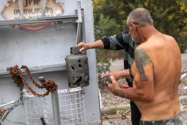 Residents check the damage to a trailer the day after a missile was intersected on the outskirts of Tel Aviv on March 14, 2026. On February 28, Israel and the United States launched strikes on Iran, killing its supreme leader and triggering a war that spread across the Middle East. (Photo by Ilia YEFIMOVICH / AFP) / 