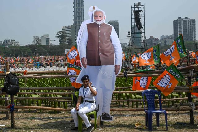 A police personnel sits near a cut-out of India's Prime Minister and Bharatiya Janata Party (BJP) leader Narendra Modi during a mass rally in Kolkata on March 14, 2026. (Photo by Dibyangshu SARKAR / AFP)