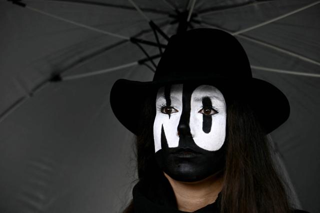 A demonstrator with her face painted in black and bearing white painted "NO" written letters protects herself from the rain under an umbrella while taking part in a rally organized by the "Social No" commitee to also mobilise support for a "No" vote in the justice referendum in Rome on March 14, 2026. (Photo by Filippo MONTEFORTE / AFP)