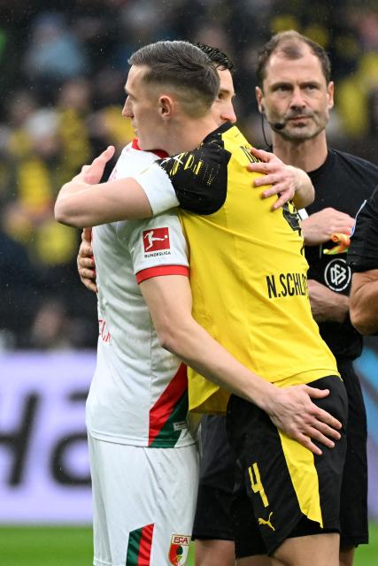 Dortmund's German defender #04 Nico Schlotterbeck (C) and brother Augsburg's German defender #31 Keven Schlotterbeck (L), who play as captains for the first time for their respective teams, hug each other prior to the German first division Bundesliga football match between BVB Borussia Dortmund and Augsburg in Dortmund, western Germany on March 14, 2026. (Photo by UWE KRAFT / AFP) / DFL REGULATIONS PROHIBIT ANY USE OF PHOTOGRAPHS AS IMAGE SEQUENCES AND/OR QUASI-VIDEO