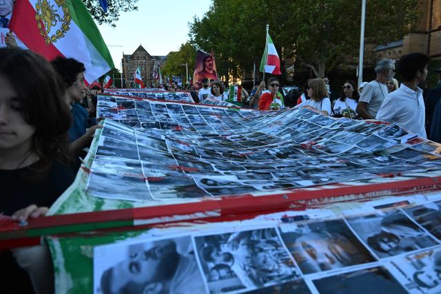 Members of the Iranian community in Australia carry a large banner bearing images of victims, during a rally following US and Israeli attacks on Iran sparking the Middle East war, in Sydney on March 14, 2026. (Photo by SAEED KHAN / AFP)