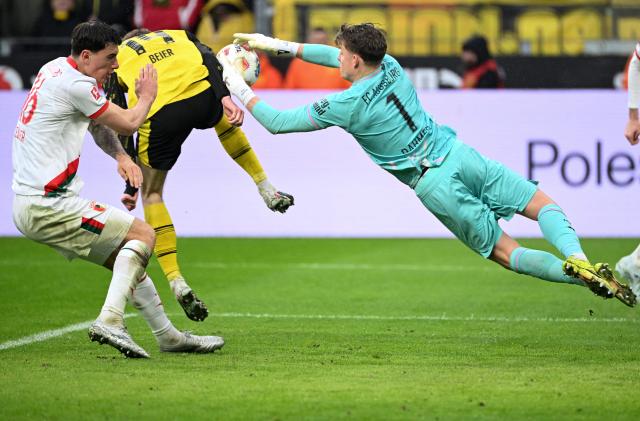 TOPSHOT - Augsburg's German goalkeeper #01 Finn Dahmen (R) makes a save during the German first division Bundesliga football match between BVB Borussia Dortmund and FC Augsburg in Dortmund, western Germany on March 14, 2026. (Photo by UWE KRAFT / AFP) / DFL REGULATIONS PROHIBIT ANY USE OF PHOTOGRAPHS AS IMAGE SEQUENCES AND/OR QUASI-VIDEO
