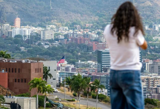 A woman stands atop a hill overlooking the US embassy in Caracas on March 14, 2026, ten days after the restoration of diplomatic relations following the capture of ousted leader Nicolas Maduro in a US military raid. (Photo by Maryorin Mendez / AFP)