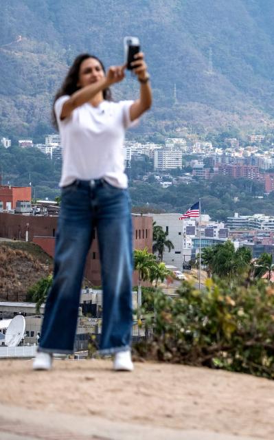 A woman poses for a selfie atop a hill overlooking the US embassy in Caracas on March 14, 2026, ten days after the restoration of diplomatic relations following the capture of ousted leader Nicolas Maduro in a US military raid. (Photo by Maryorin Mendez / AFP)