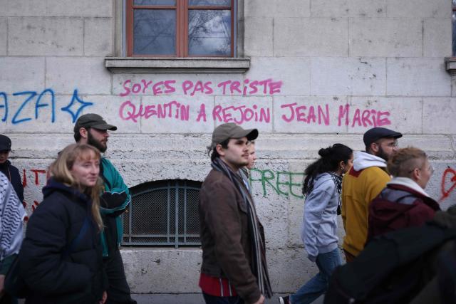 Protesters walk past graffiti reading "Don’t be sad, Quentin has joined Jean-Marie" during a march to protest against racism and fascism in Lyon, southeastern France, on March 14, 2026. Some 85 rallies have been announced throughout France for March 14, on the eve of a highly uncertain local election. The vote serves as a test one year ahead of the 2027 presidential election, particularly for the far right, which hopes to build on its momentum. (Photo by Alex MARTIN / AFP)