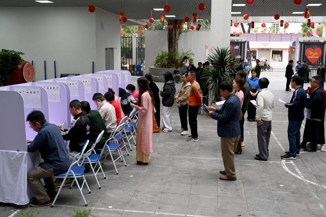 People fills out their ballot at a voting station in Hanoi on March 15, 2026. Polls opened in Vietnam with voters casting ballots for members of the National Assembly, the country's top legislative body that serves mainly to ratify decisions by the ruling Communist Party. (Photo by Nhac NGUYEN / AFP)