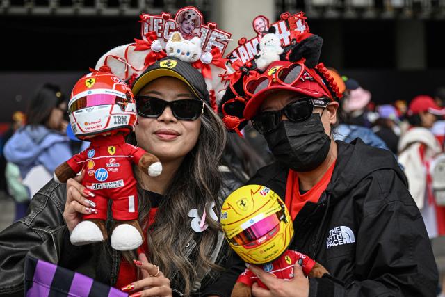 Fans wearing headbands featuring team Ferrari's Monegasque driver Charles Leclerc (L) and British driver Lewis Hamilton pose for photos prior to the Formula One Chinese Grand Prix at the Shanghai International Circuit in Shanghai on March 15, 2026. (Photo by Jade GAO / AFP)