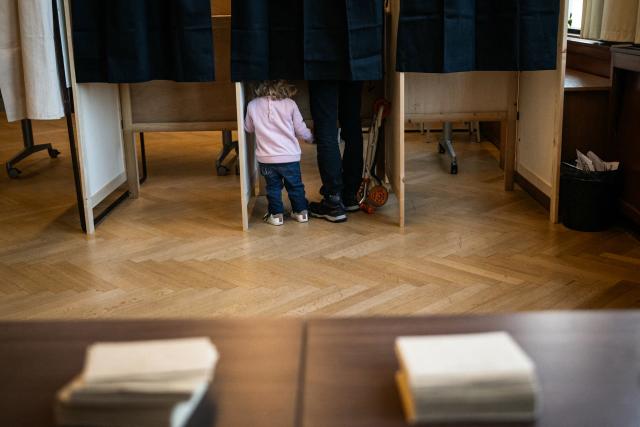 A child stands in a polling booth as the father casts his ballot during the first round of France's 2026 municipal elections in Lyon, central eastern France, on March 15, 2026. (Photo by ARNAUD FINISTRE / AFP)