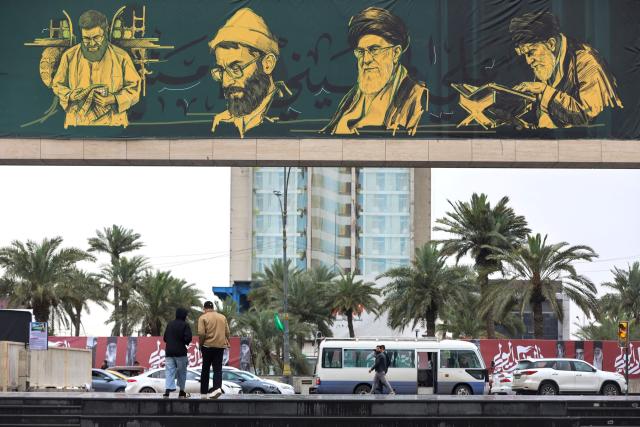 Iraqis walk past a large banner depicting Ayatollah Ali Khamenei, Iran's late supreme leader who was killed on February 28 in a US-Israeli strike in Tehran, displayed at Baghdad's central Tahrir Square on March 15, 2026. Iraq, long a proxy battleground between the United States and Iran, was quickly dragged into the Middle East war triggered by US and Israeli strikes on Iran on February 28 . (Photo by AHMAD AL-RUBAYE / AFP) / 