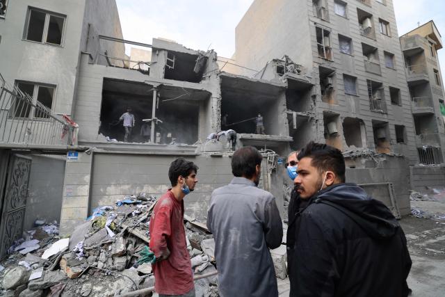Iranians look on as others clear the debris from damaged homes in the Iranian capital Tehran on March 15, 2026. Iran's Foreign Minister said in an interview published on March 15, that the war pitting his country against the United States and Israel will only end when Tehran can be certain it will not be restarted (Photo by Atta KENARE / AFP) / 