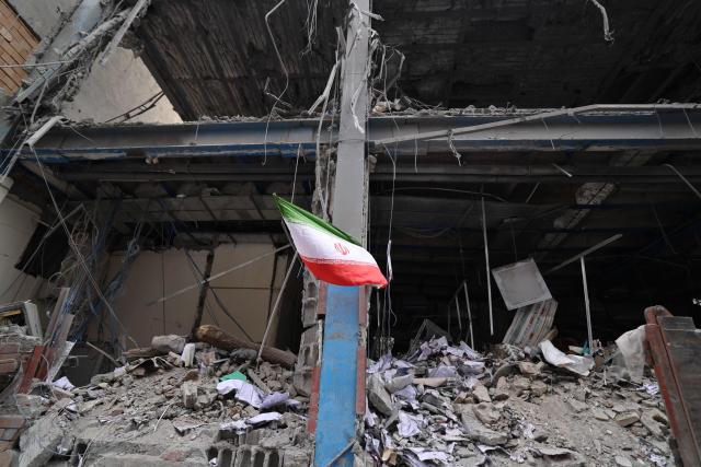 An Iranian flag flutters outside a destroyed building in the Iranian capital Tehran on March 15, 2026. Iran's Foreign Minister said in an interview published on March 15, that the war pitting his country against the United States and Israel will only end when Tehran can be certain it will not be restarted (Photo by Atta KENARE / AFP) / 
