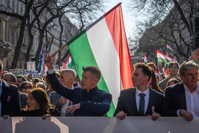 Hungarian opposition leader and president of the TISZA (Respect and Freedom) party Peter Magyar (C-L) raises a national flag of Hungary as he marches alongside protesters during a "National March” in Budapest, Hungary on March 15, 2026, on the 178th anniversary of the Hungarian Revolution and War of Independence of 1848-1849. The 1848-1849 revolution in the Kingdom of Hungary grew into a war for independence from the Austrian Empire, ruled by the Habsburg dynasty. (Photo by Ferenc ISZA / AFP)
