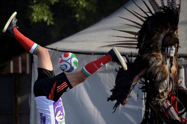 A young man does pull-ups with a ball before the start of a world-class football clinic at the Zocalo square in Mexico City on March 15, 2026, aimed at setting a new Guinness World Record. (Photo by Alfredo ESTRELLA / AFP)