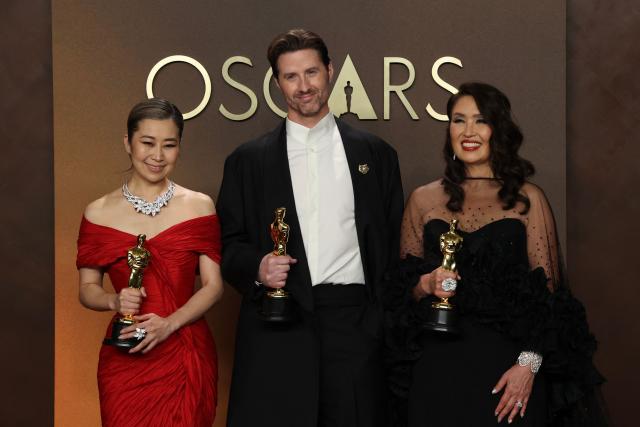 (L/R) South Korean-Canadian storyboard artist and writer, US film director Chris Appelhans, and film producer Michelle Wong pose in the press room with the Oscar for Best Animated Feature Film for "KPop Demon Hunters" during the 98th Annual Academy Awards at the Dolby Theatre in Hollywood, California on March 15, 2026. (Photo by VALERIE MACON / AFP)