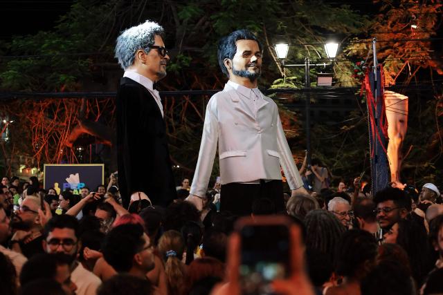 Giant puppets depicting Brazilian film director Kleber Mendonca Filho and actor Wagner Moura of the film "O Agente Secreto" are seen outside the Sao Luiz cinema in Recife, Brazil on March 15, 2026. Brazilians all over the country are gathered expecting the result of the nominations of the Brazilian film "O Agente Secreto" (The Secret Agent). (Photo by BRENDA ALCANTARA / AFP)