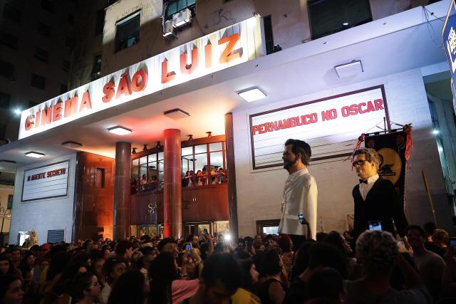 Giant puppets depicting Brazilian film director Kleber Mendonca Filho and actor Wagner Moura of the film "O Agente Secreto" are seen outside the Sao Luiz cinema in Recife, Brazil on March 15, 2026. Brazilians all over the country are gathered expecting the result of the nominations of the Brazilian film "O Agente Secreto" (The Secret Agent). (Photo by BRENDA ALCANTARA / AFP)