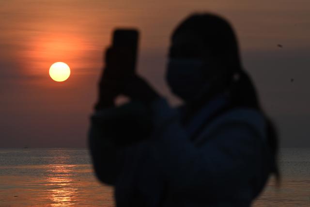 A woman takes pictures of the sunrise during a Melasti ceremony prayer at a beach in Denpasar on Indonesia's resort island of Bali on March 16, 2026. Melasti is a purification festival which is held several days before "Nyepi", the day of silence, when Hindu devotees are not allowed to work, travel or take part in any indulgence (Photo by SONNY TUMBELAKA / AFP)