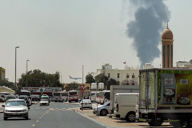 TOPSHOT - An Emirates aircraft lands as a smoke plume rises from an ongoing fire at Dubai International Airport in Dubai on March 16, 2026. Flights were gradually resuming at Dubai airport on March 16, previously the world's busiest for international flights, the airport operator said, after a "drone-related incident" sparked a fuel tank fire nearby, as Iran kept up its Gulf attacks. (Photo by AFP) / 
