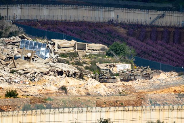 Israeli army fighting vehicles manoeuver across the border inside a destroyed Lebanese village as seen from the Upper Galilee in northern Israel on March 16, 2026. The Israeli military said on March 16 that it had begun what it described as "limited ground operations" against Hezbollah in southern Lebanon. Lebanon was drawn into the Middle East war on March 2 when the Tehran-backed Hezbollah attacked Israel in response to the killing of the Iranian supreme leader in US-Israeli strikes, with Israel launching air raids on the neighbouring country and troop incursions into border areas. (Photo by Odd ANDERSEN / AFP) / 