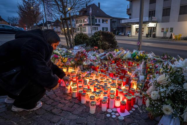 A women places lights a candle at the site where a bus from the public transport company PostBus caught fire last week after a man described as "disturbed" set himself alight, killing at least six people, including the perpetrator, and injuring five others, in Kerzers, western Switzerland, on March 16, 2026. Investigators said that the suicide hypothesis remains the most likely. (Photo by Fabrice COFFRINI / AFP)