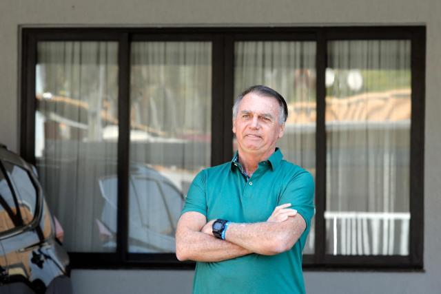 (FILES) Former Brazilian President Jair Bolsonaro gestures at the garage of his residence in Brasilia on September 11, 2025. Imprisoned former Brazilian president, Jair Bolsonaro, continued to show signs of improvement at the hospital where he is being treated for pneumonia, and has been moved from intensive care to a "semi-intensive" care unit, his wife reported on March 16, 2026. (Photo by Sergio Lima / AFP)