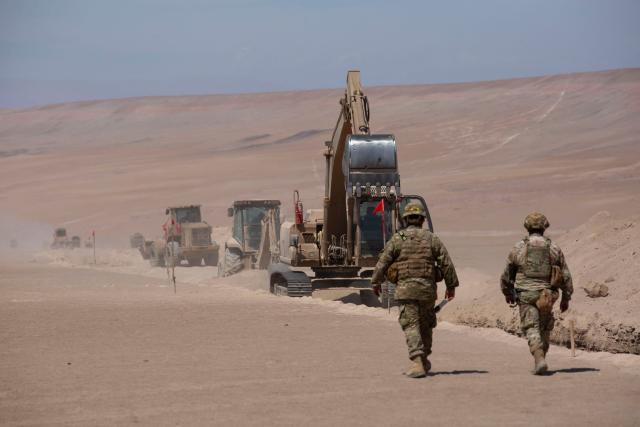 Two soldiers stand guard as heavy machinery operates near the Chacalluta border post along the Chile–Peru border on March 16, 2026. Chile's President Jose Antonio Kast launched a border trench project to curb illegal migration. (Photo by Patricio BANDA / AFP)
