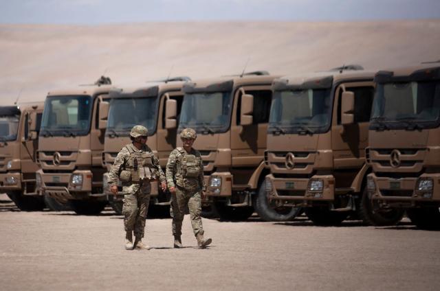 Two soldiers stand guard next to trucks near the Chacalluta border post along the Chile–Peru border on March 16, 2026. Chile's President Jose Antonio Kast launched a border trench project to curb illegal migration. (Photo by Patricio BANDA / AFP)