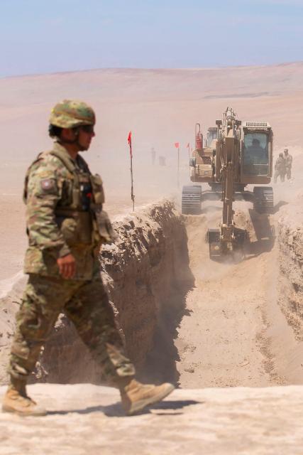 A soldier stands guard as heavy machinery operates near the Chacalluta border post along the Chile–Peru border on March 16, 2026. Chile's President Jose Antonio Kast launched a border trench project to curb illegal migration. (Photo by Patricio BANDA / AFP)