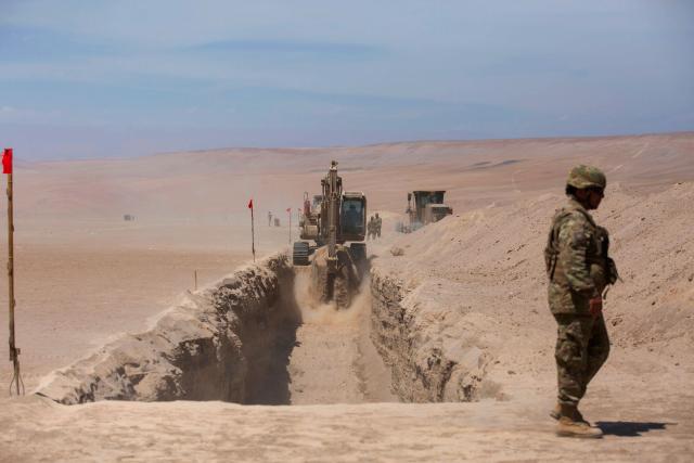 A soldier stands guard as heavy machinery operates near the Chacalluta border post along the Chile–Peru border on March 16, 2026. Chile's President Jose Antonio Kast launched a border trench project to curb illegal migration. (Photo by Patricio BANDA / AFP)