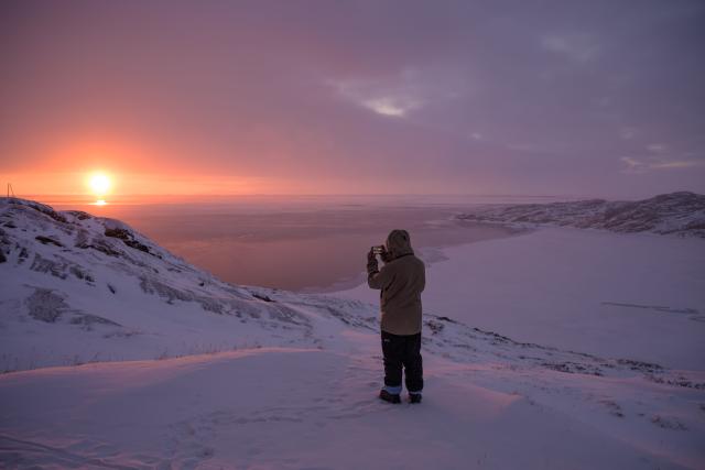 A boy takes a photo of the sunset, with the icy bay in the background, in Ilulissat, Greenland, on March 16, 2026. (Photo by Florent VERGNES / AFP)