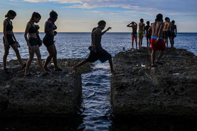 A group of young people enjoy a sunset on the Malecon during a blackout in Havana on March 16, 2026. Cuba suffered a widespread power cut on March 16, 2026, according to the national electricity company, against the backdrop of a severe crisis on the island caused by the US energy blockade. (Photo by Yamil LAGE / AFP)