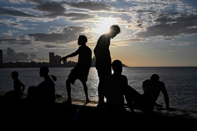 TOPSHOT - A group of young people enjoy a sunset on the Malecon during a blackout in Havana on March 16, 2026. Cuba suffered a widespread power cut on March 16, 2026, according to the national electricity company, against the backdrop of a severe crisis on the island caused by the US energy blockade. (Photo by Yamil LAGE / AFP)