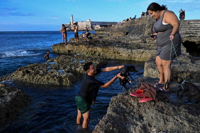A man pulls a dog out of the sea at sunset on the Malecon during a blackout in Havana on March 16, 2026. Cuba suffered a widespread power cut on March 16, 2026, according to the national electricity company, against the backdrop of a severe crisis on the island caused by the US energy blockade. (Photo by Yamil LAGE / AFP)