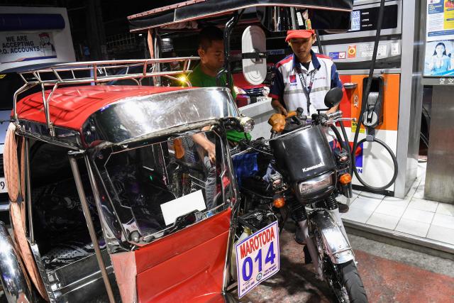 A petrol station employee fills up a tricycle with gasoline prior to a fuel price increase in Manila on March 17, 2026. Oil climbed again in Asia on March 17 after prices retreated a day earlier, with investors remaining focused on the Strait of Hormuz. (Photo by Ted ALJIBE / AFP)